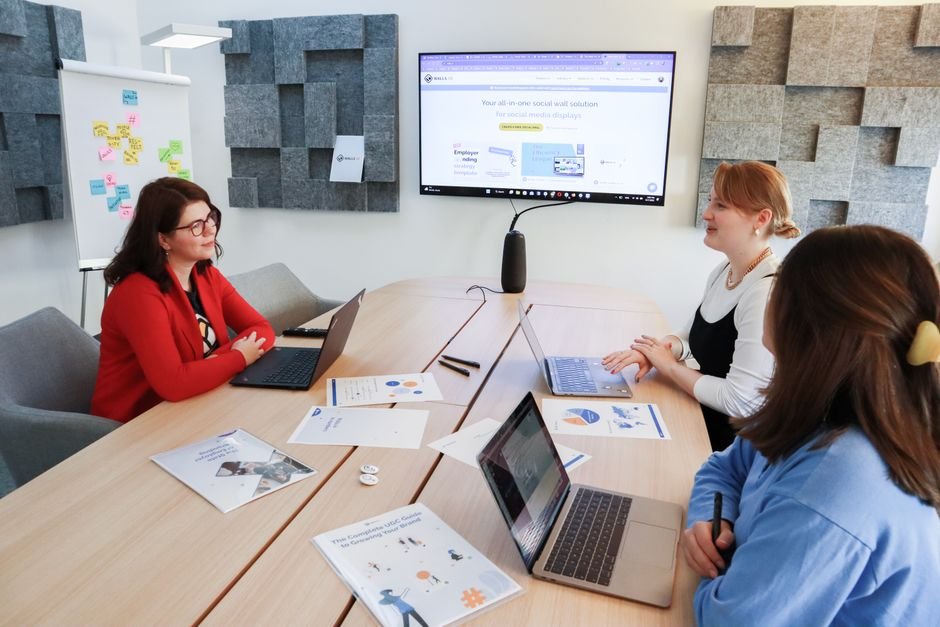 Business meeting with three women discussing strategies using laptops and presentations in a modern office.