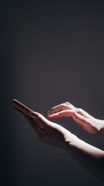 Close-up of hands holding a smartphone under dramatic lighting, highlighting modern technology use.
