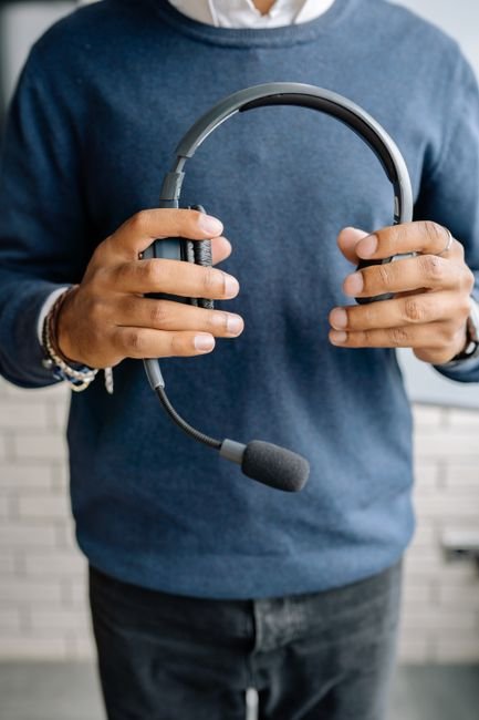 Close-up of a person wearing a blue sweater holding a headset with both hands.