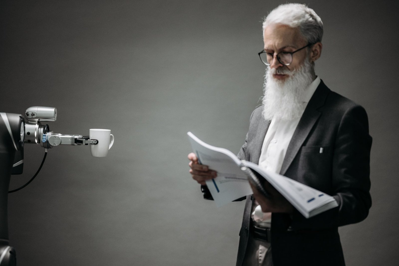 A robot arm assists a professional with a book and coffee in a modern office setup. Technology meets innovation.