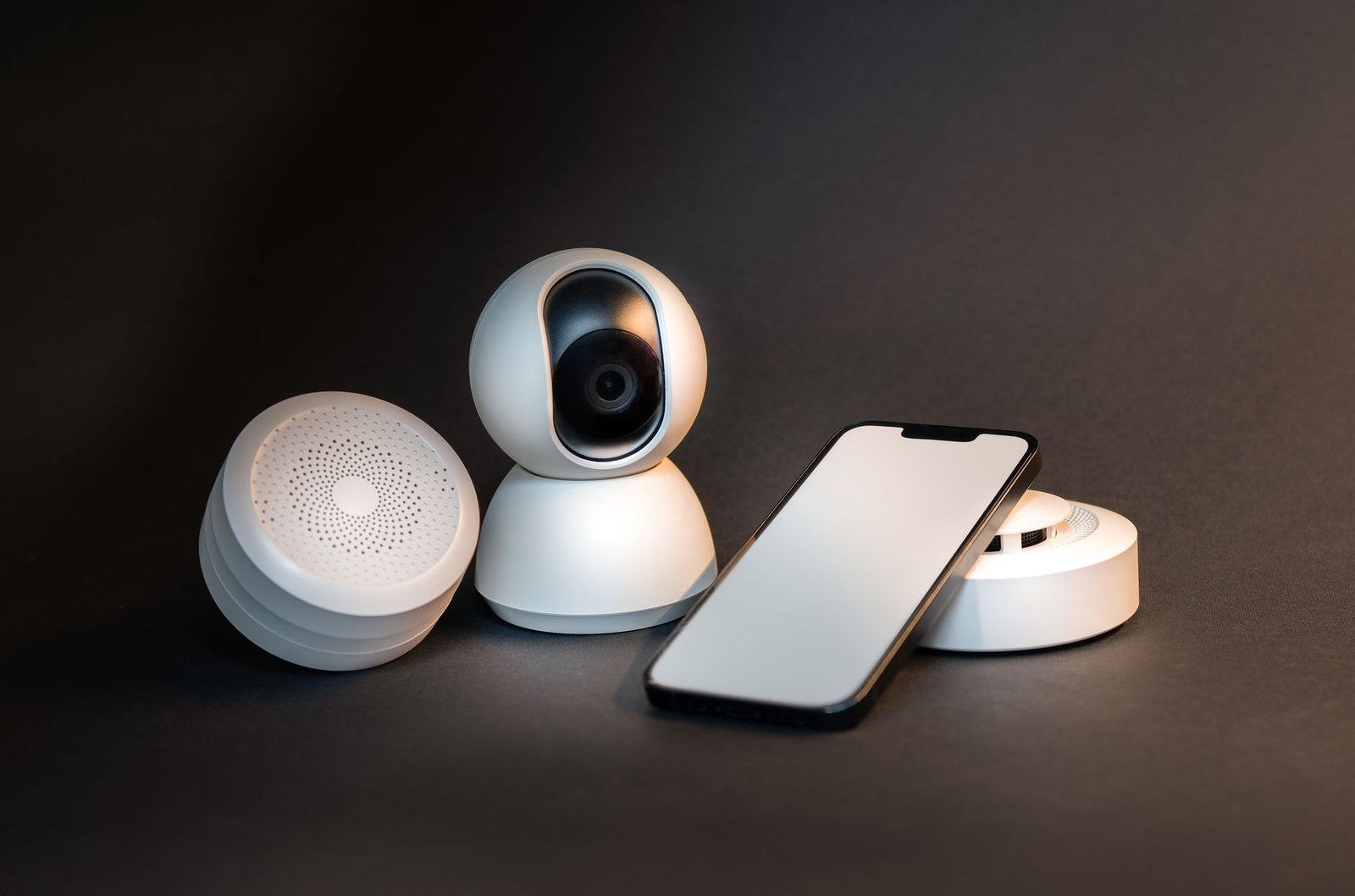 A sleek smartphone with modern smart home devices on a minimalist gray background.